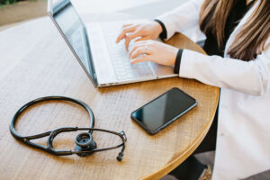 Primary care clinician at a laptop with stethoscope and phone, illustrating how an HSA works with Direct Primary Care